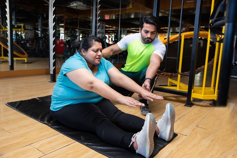 A trainer assisting a woman exercising in a gym